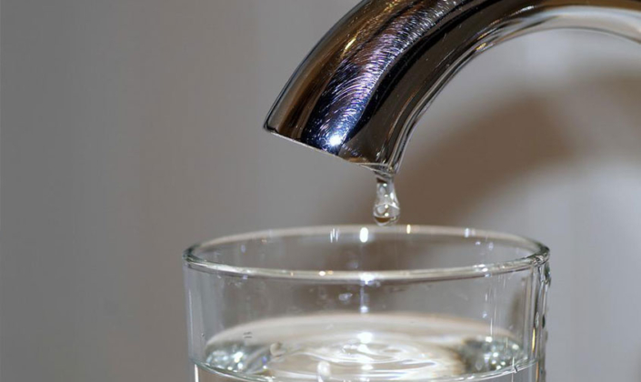 Close up image of a tap with a drop of water falling into a glass