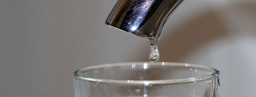 Close up image of a tap with a drop of water falling into a glass